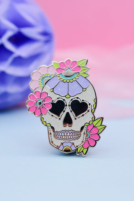 Colorful sugar skull-shaped pin with floral details on a pastel background